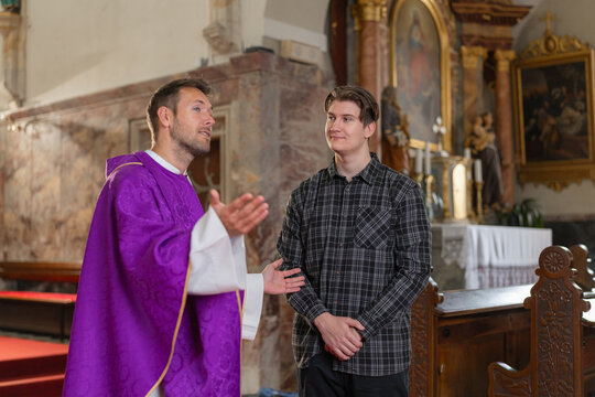 A young man student and a catholic priest engage in conversation inside a church about christian beliefs and faith.