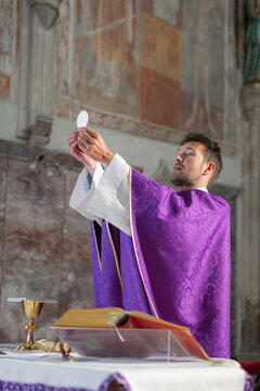 Catholic priest is leading a holy mass in a church. He holds up the host during the eucharistic celebration.