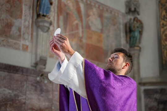A catholic priest performs a holy mass in a church. He holds up the host to the congregation as part of the religious ceremony.