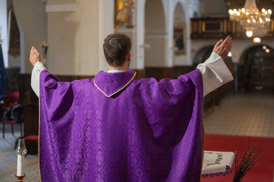 Catholic priest raises his arms during a church ceremony of holy mass. The setting is a Catholic church with religious decorations.