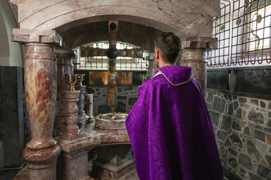 A catholic priest stands before the altar in a church ready to conduct a holy mass. The setting includes religious symbols and decor.
