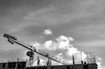 Black and white silhouette of tower crane and workers on top of concrete building under construction with sky background © LemPro Filming Life