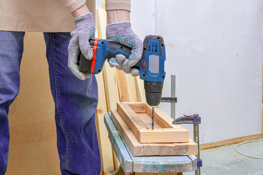 Person drilling timber with a cordless power drill at a woodworking bench. Carpentry and DIY home improvement. Construction, repair and woodworking projects. Hands-on workshop craft
