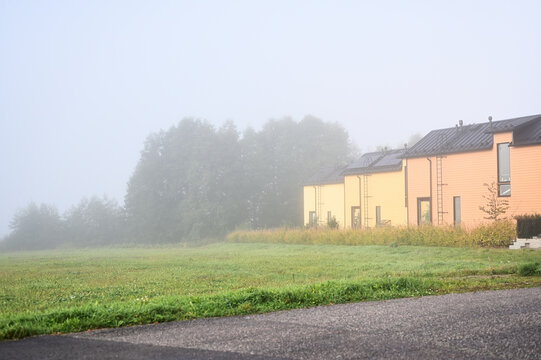 A row of modern yellow wooden houses beside a grassy field on a misty autumn morning