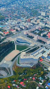 Vertical video. Ufa, Russia. Aerial panorama over the central cityscape at twilight, modern curved facades and dense residential blocks fading into the soft post-sunset haze. Drone footage. Rich colo