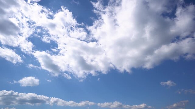 Time lapse of fluffy white clouds moving across a bright blue sky, large cumulus clouds overhead and a row of smaller clouds along the horizon