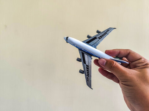 Close-up of a hand holding a small toy airplane against a clean light background, representing travel and summer vacation concepts.   