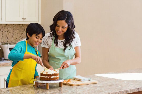 Mother and son frosting a carrot cake in a sunny kitchen