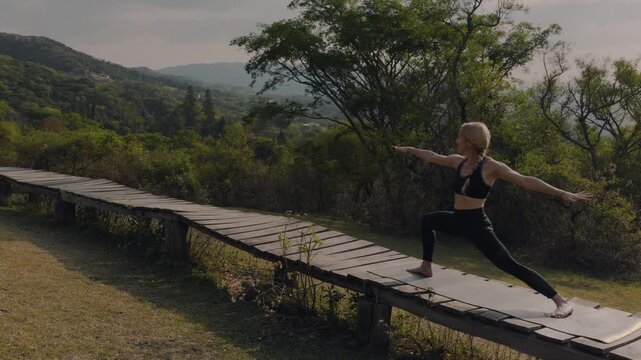 Woman flows from warrior pose into a twisting side plank on a mountain boardwalk