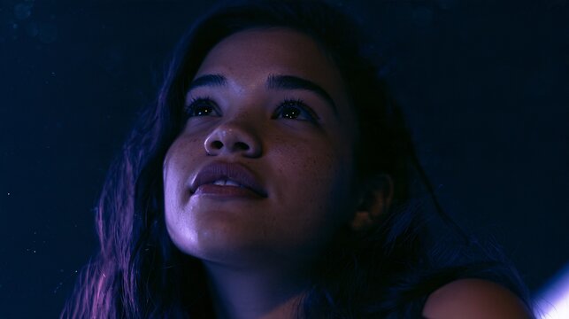 Close-up portrait of a young woman gazing upward in wonder, illuminated skin with faint freckles