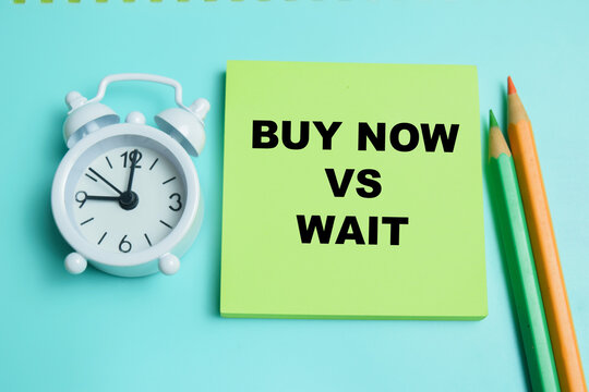 Concept of buy now vs wait write on sticky notes isolated on table.