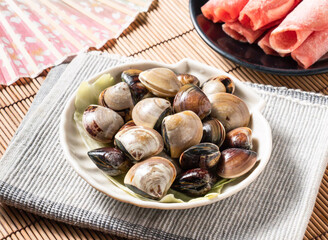 Fresh raw clams served in a shell shaped bowl on a bamboo mat © Sana