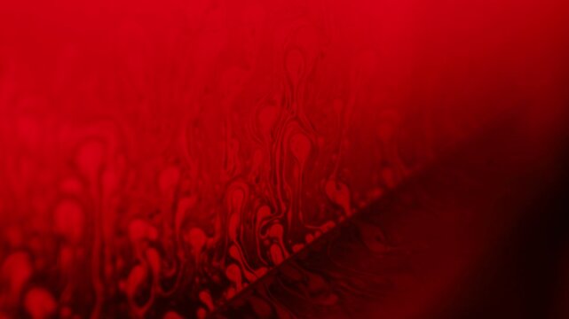 Intense crimson red liquid film horizon with rising convection plumes and diagonal rim. A low-key macro photograph capturing a liquid film surface illuminated in deep crimson red backlight