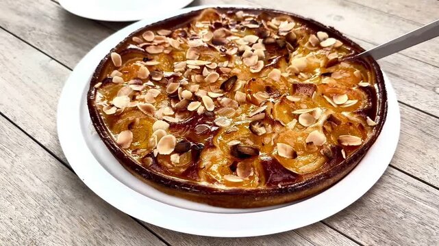  Hand cutting a freshly baked apricot tart with sliced almonds