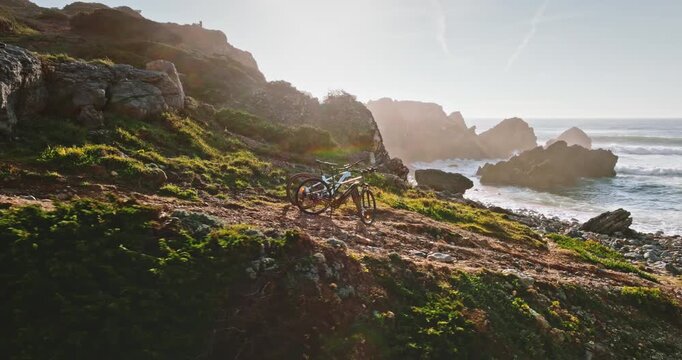 Two mountain bikes are resting on a rugged trail overlooking the Atlantic Ocean and rocky cliffs, symbolizing outdoor adventure, sports and exploration along stone coast at sunrise. Portugal, Lisbon