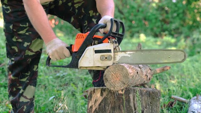 Worker using a chainsaw to cut a log on a tree stump in a green outdoor woodland setting