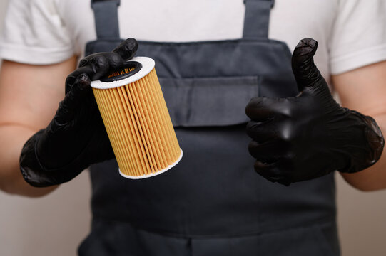 Mechanic showing thumbs up gesture holding new car oil filter cartridge. Auto repair service approval, regular vehicle engine maintenance, professional garage worker and quality part concept.