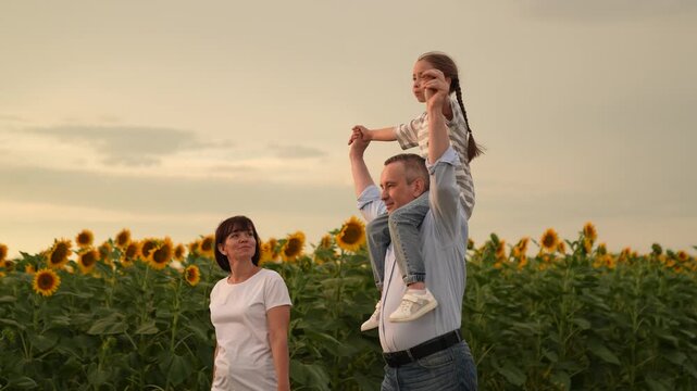 Happy family in sunflower field, Father carrying daughter on shoulders, Mother smiling at family, Joyful summer evening outdoors, Family bonding and fun, Parenthood and childhood moments, Sunflower