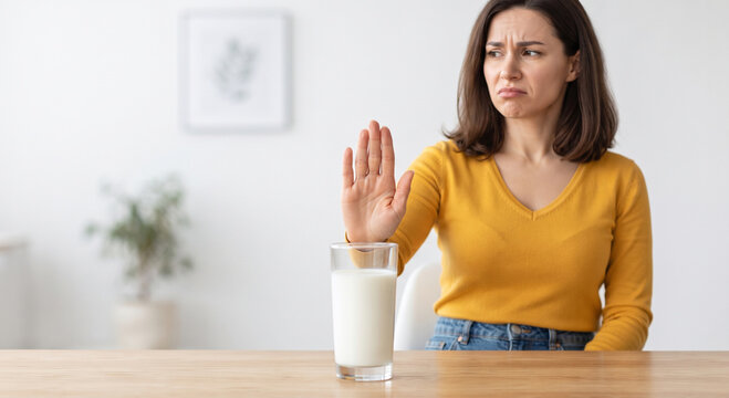 Woman making stop gesture rejecting glass of milk showing dairy intolerance