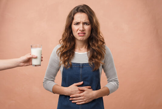 Woman holding stomach in pain rejecting glass of milk representing lactose intolerance