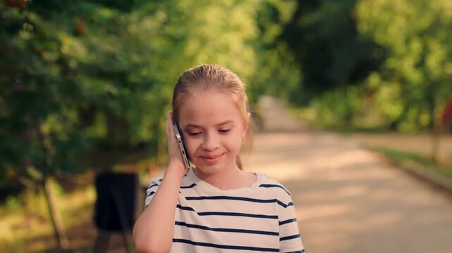 cute girl holding smartphone in green park, girl answering call in peaceful park, kid smiling while talking on phone outside, happy kid on phone during outdoor walk, adorable child with smartphone in
