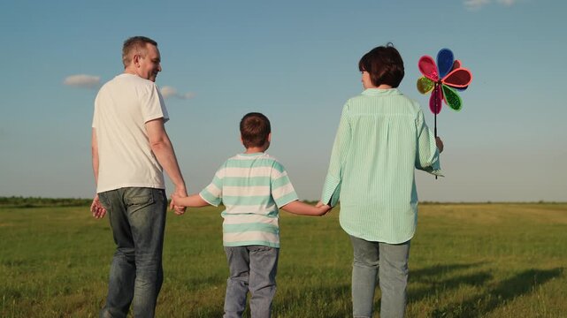 boy Child kid mother father child walking sunset park, parents children walking run holding hands, children playing colorful pinwheel, mother and father, tranquil outdoor scene, sunny countryside day