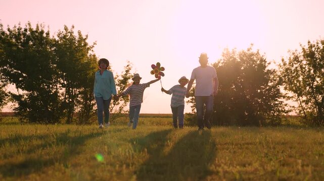 boy girl Child kid mother father child walking sunset park, parents children walking run holding hands, children playing colorful pinwheel, grass underfoot running, field at sunset, kids leading