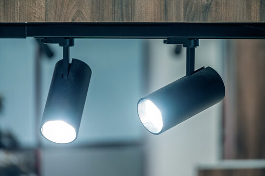 Black ceiling spotlights hanging from a track system, providing focused illumination in a contemporary indoor space