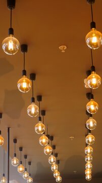 Rows of glowing pendant bulbs extend along a high ceiling in a vertical interior view. Repetitive warm lighting represents perspective, symmetry and contemporary architectural atmosphere