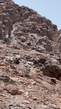 Rugged rocky desert mountain with wire fence under clear sky in Saudi Arabia.