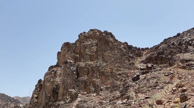 Rugged rocky desert mountain and wire fence under a clear sky in Saudi Arabia.