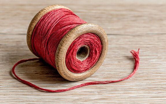Top-down view of a single vintage wooden spool of crimson red sewing thread on a light oak table