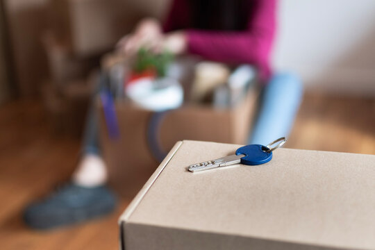 Young woman packing cardboard boxes with a new house key on top, symbolizing moving day, independence, starting a new home and personal growth toward autonomy and freedom