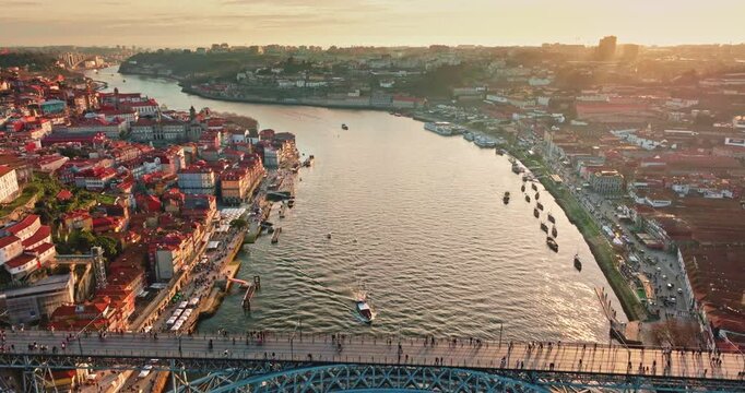 Dom Luis I bridge crosses the Douro River, connecting the historic districts of Porto and Vila Nova de Gaia with a busy pedestrian deck and lower traffic level at golden hour sunset light. Aerial shot