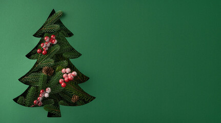 Fototapeta premium Minimal green Christmas tree cutout with frosted berries and pinecones for New Year greeting on banner green background