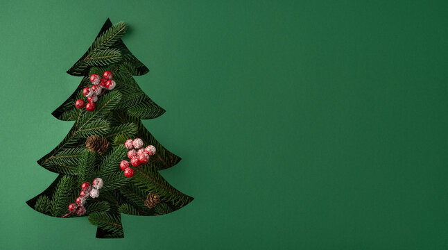 Minimal green Christmas tree cutout with frosted berries and pinecones for New Year greeting on banner green background