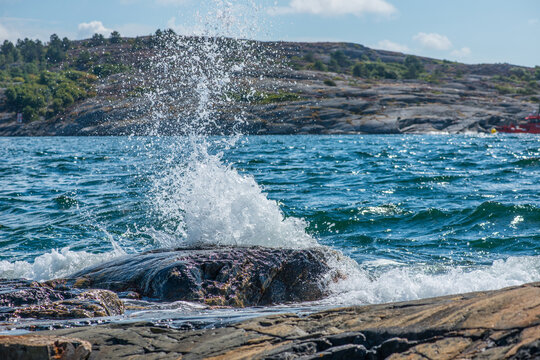Powerful sea wave splashing dramatically against rocky Swedish shoreline.