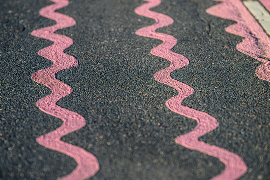 Pink wavy markings form repeating abstract pattern on asphalt pavement.