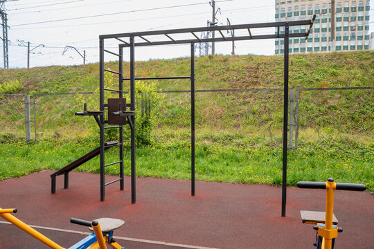 Outdoor street workout station with pull-up bars, ladder and parallel bars. Public calisthenics equipment for strength training and bodyweight exercise. Urban fitness area beside railway