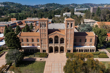 Naklejka na ściany i meble Aerial view of the historic brick facade of Royce Hall on the UCLA university campus in Los Angeles, California, with courtyards and surrounding trees under bright sunlight.