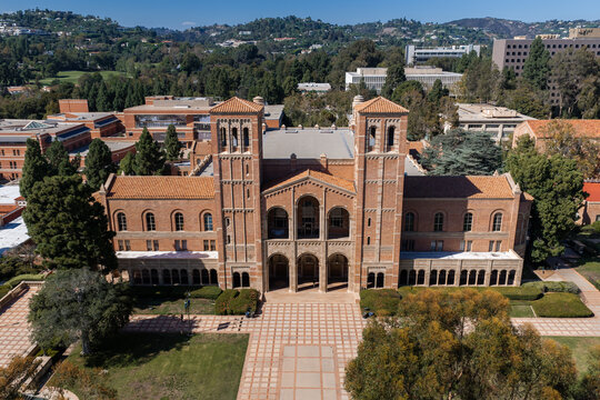 Aerial view of the historic brick facade of Royce Hall on the UCLA university campus in Los Angeles, California, with courtyards and surrounding trees under bright sunlight.