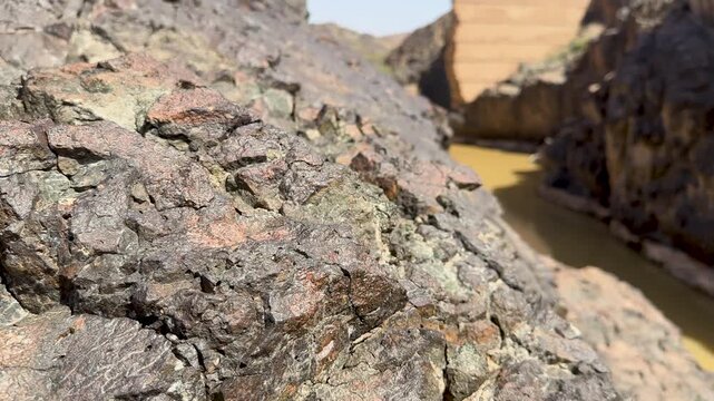 Close up of dark rocks revealing a broken ancient dam and muddy river gorge in Saudi Arabia.