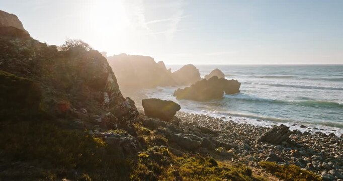 Mountain bike resting on a rocky coastal path overlooking the Atlantic Ocean with waves crashing against dramatic cliffs and golden sunlight illuminating the rugged landscape near Lisbon, Portugal