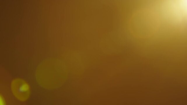 Warm golden lens flares and soft light leaks create an abstract glowing background with optical texture for cinematic overlays, transitions and compositing.