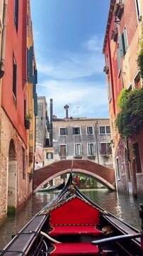 Tracking shot of gondola gliding through narrow canal in Venice under sunny sky