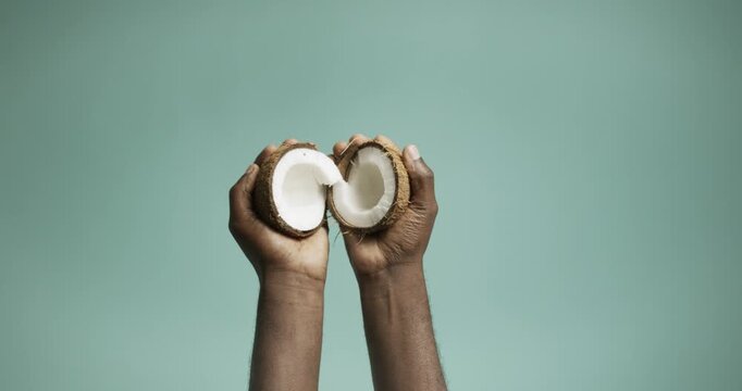 Hands Holding Two Fresh Coconut Halves Against a Green Background