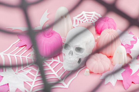 Pink Halloween flat lay with pumpkins, cute ghosts, artificial skull, bats and spider webs