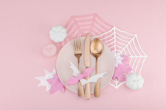 Pink Halloween table setting flat lay with plate, cutlery on rosy background