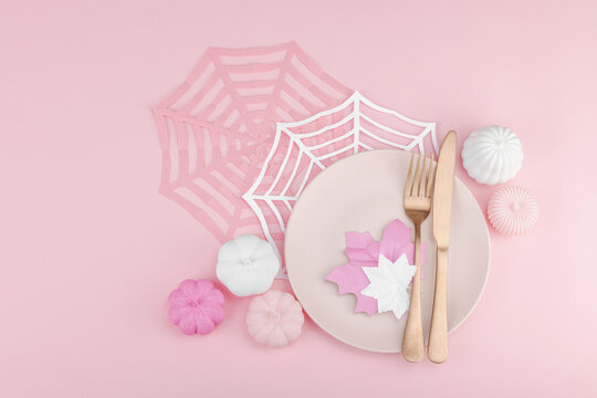 Pink Halloween table setting flat lay with plate, cutlery on rosy background