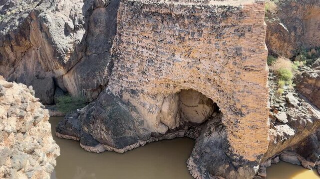 High angle view of ancient dam ruins and a muddy wadi in a Saudi canyon.